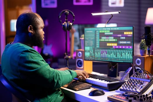 Sound engineer recording piano notes with DAW software in his home studio, working at night on producing new music with electronic tools. Musician composing tunes on midi controller.