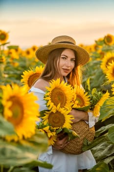 A girl in a hat on a beautiful field of sunflowers against the sky in the evening light of a summer sunset. Sunbeams through the flower field. Natural background