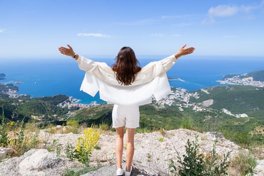 Young beautiful woman stands with her back and looks at the old town of Budva, Montenegro