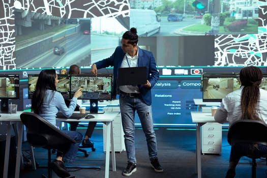 Indian coordinator offers instructions for his staff in control center monitoring room, following delivery trucks with gps coordinates on satellite map. Agency employees provide support for couriers.