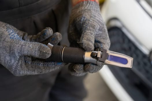 A mechanic holds a Refractometer in a car service center. Portable optical device for determining the freezing point of antifreeze