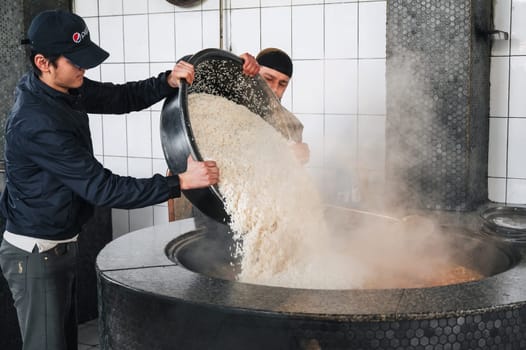 male chefs pour rice for traditional Uzbek pilaf into a cauldron in kitchen in Central Asian Pilaf Center Besh Qozon. Tashkent, Uzbekistan - April 16, 2024