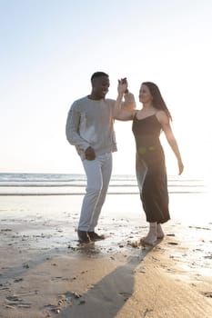 A man and woman are dancing on the beach. The man is wearing a white shirt and the woman is wearing a black dress. Scene is lighthearted and fun, as the couple is enjoying themselves on the beach