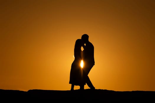 A couple is kissing in the sun, with the sun shining on them. The image has a romantic and intimate mood