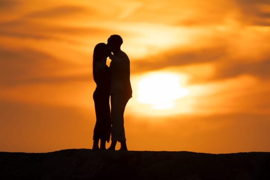 A couple is kissing in front of a sunset. Scene is romantic and intimate