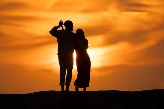 A couple standing on a hillside at sunset, with the woman hugging the man. Scene is romantic and peaceful