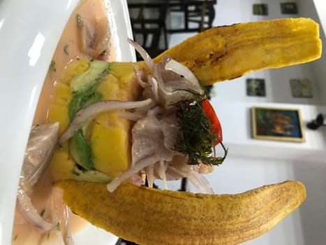 Overhead shot of traditional ceviche served with ripe plantain on a white bowl