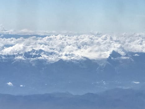 Aerial view showing the top of snow-capped mountains emerging from fluffy clouds