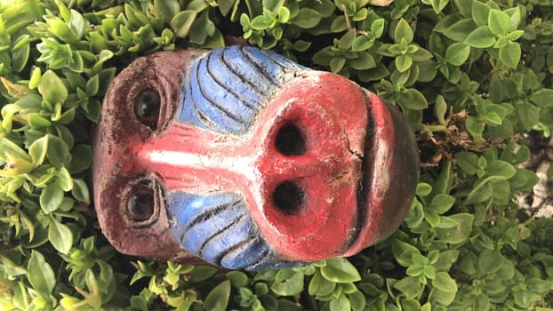Vibrant tribal mask nestled in lush green foliage, showcasing artistic garden decor