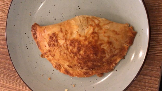 Top view of a deliciously baked calzone with a crisp crust, served on a grey plate