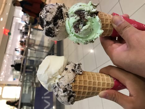 Close-up of hands holding three different flavored ice cream cones indoors
