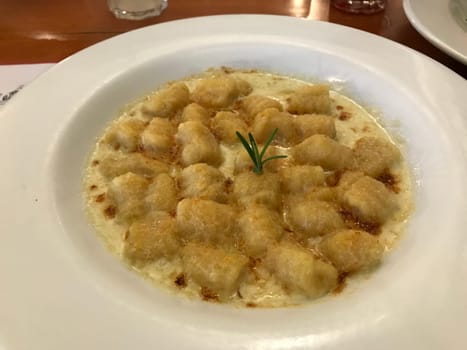 Delicious cooked gnocchi with creamy sauce garnished with herbs, served in a white dish