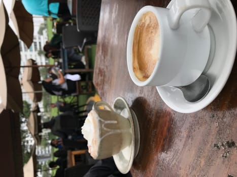 Enjoying a leisurely and cozy coffee break outdoors at a charming cafe with a wooden table, blurred background, and a delicious espresso or cappuccino topped with whipped cream