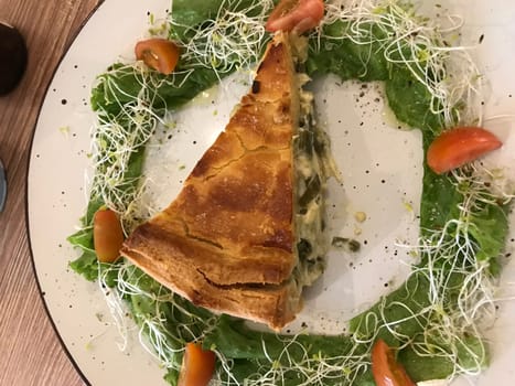 Freshly baked spinach quiche served with sprouts and cherry tomatoes on a white plate