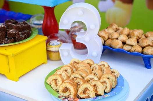 Colorful table with desserts featuring a number 3 decoration at a toddler's birthday celebration