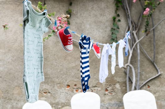 Assortment of infant clothing and tiny sneakers hanging on a washing line with a garden backdrop