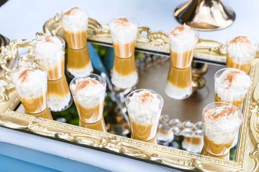 Gourmet dessert shots with cream topping on a luxurious gold mirror tray, ideal for events