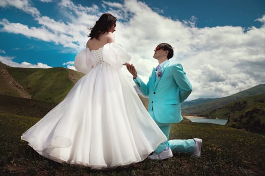 A beautiful wedding couple hugs tenderly against the backdrop of a mountain river and lake, the bride's long white dress.