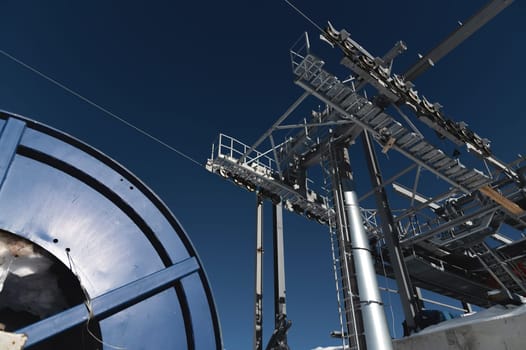 A cable car station under construction high in the mountains in winter. Focus on a close-up of a thick cable car cable covered with snow.