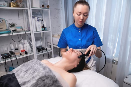 Lymphatic drainage massage is a hardware process. A cosmetologist-therapist gives a model a rejuvenating facial massage in a beauty salon. Close-up.