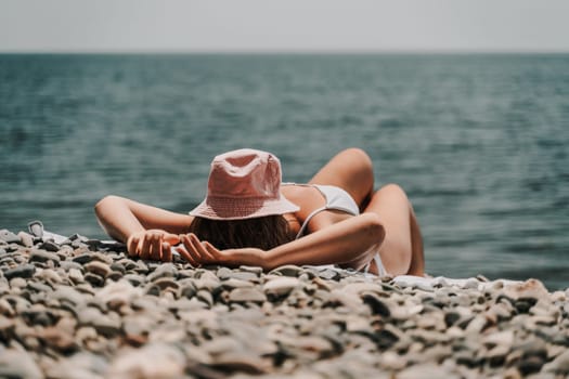 A woman is laying on the beach with a pink hat on her head. She is wearing a white bikini and is relaxing in the sun