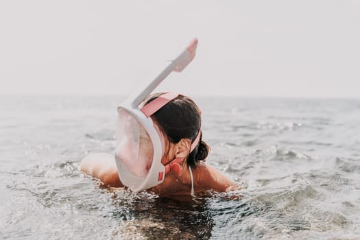 A woman is swimming in the ocean wearing a pink snorkel. The water is calm and the sky is clear