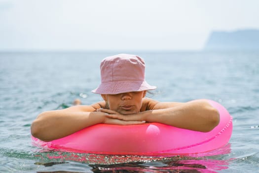 A woman is floating on a pink inflatable raft in the ocean. She is wearing a pink hat and a black bikini top. The scene is peaceful and relaxing, with the woman enjoying the water and the sun
