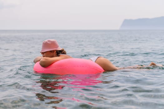 A woman is floating on a pink inflatable raft in the ocean. The water is calm and the sky is cloudy. The woman is wearing a white bikini and a pink hat