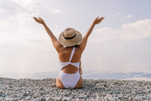 A woman wearing a straw hat and a white bikini is sitting on a beach. She is smiling and she is enjoying her time