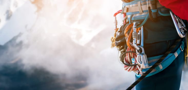 Young man traveler alpinist climbs to the top of a snowy mountain with climbing equipment, harness, carabiners, rope, a beautiful view on the background.