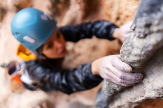 Young girl is engaged in extreme sports, fearlessly climbs up the rock using white magnesia powder, holds her hand to the ledge in the relief, close-up view, focus on the finger, the girl is blurred.