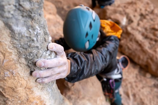 Young girl is engaged in extreme sports, fearlessly climbs up the rock using white magnesia powder, holds her hand to the ledge in the relief, close-up view, focus on the finger, the girl is blurred.