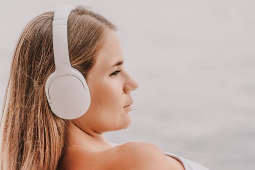 A woman wearing headphones is sitting on a beach. She is looking at the water and she is enjoying the moment