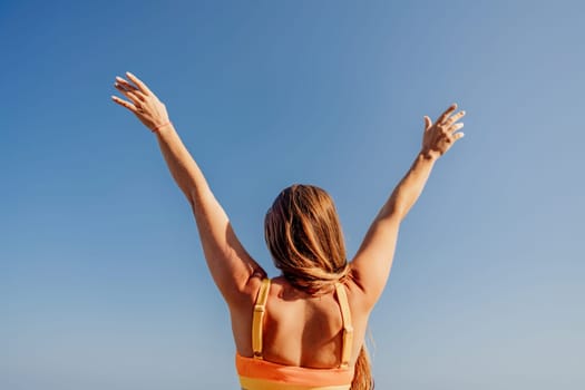 A woman with long hair is standing in the sun and is reaching up with her arms outstretched