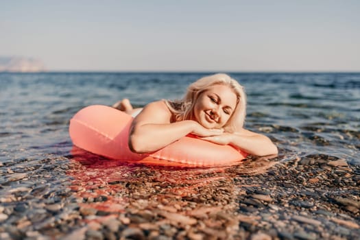 A woman is laying on a pink inflatable raft in the ocean. She is smiling and she is enjoying her time