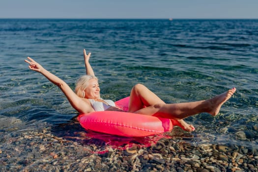 A woman is floating on a pink inflatable raft in the ocean. She is smiling and she is having a great time