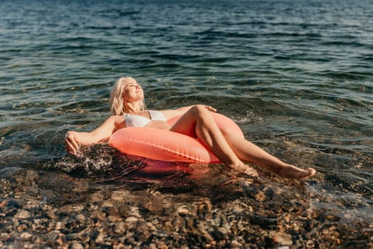 A woman is floating on a red inflatable raft in the ocean. She is wearing a white bikini and she is enjoying the water