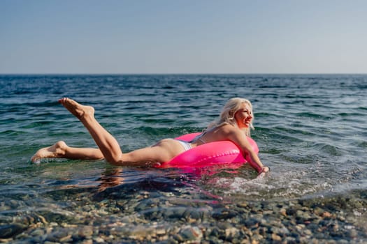 A woman in a pink float is in the ocean. The water is blue and the sky is clear