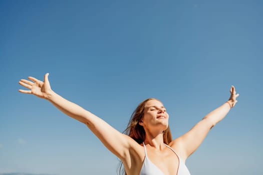 A woman is standing in the sun with her arms outstretched, looking up at the sky. She is happy and content, enjoying the beautiful day