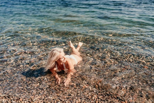 A woman is laying in the water at the beach. She is wearing a bikini and she is enjoying herself. The water is calm and clear, and the beach is rocky. The scene is peaceful and relaxing