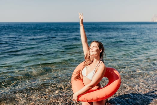 A woman is in the ocean with a red float on her head. She is smiling and making a peace sign