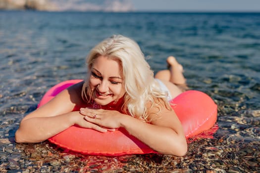 A woman is laying on a red inflatable raft in the ocean. She is smiling and enjoying the sun