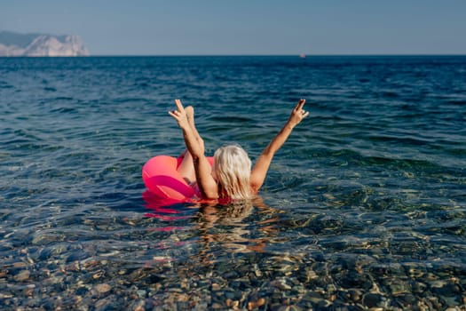 A woman in a red bikini is in the ocean, holding her hands up in the air. She is surrounded by rocks and the water is clear