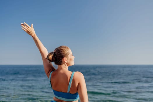 A woman is standing on the beach with her arms raised in the air. The sky is clear and blue, and the ocean is calm. The woman is enjoying the beautiful day and the peaceful surroundings