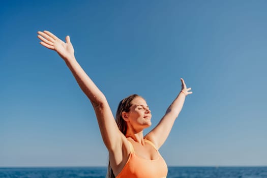 A woman is standing on the beach with her arms raised in the air, smiling and enjoying the beautiful blue sky