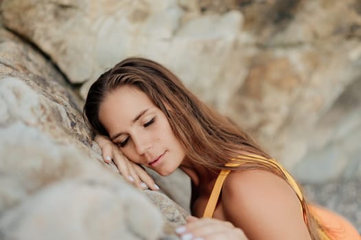 A woman in a yellow tank top is laying on a rock. She is looking at the camera with a peaceful expression