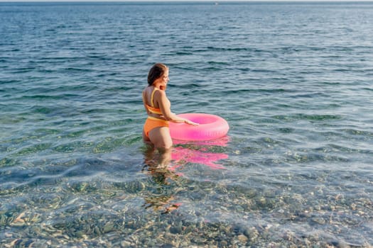 A woman in a yellow bikini is holding a pink inflatable ring in the ocean. The scene is bright and cheerful, with the woman enjoying her time in the water