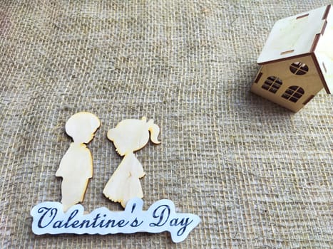 Wooden figurines of a couple, a house and the inscription Valentine's Day. The concept of a holiday of love and lovers. Background, texture, place for text and copy space