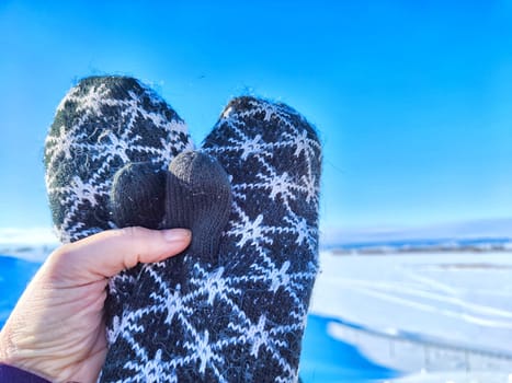 A hand with patterned woolen mittens gives thumbs up against a clear, snowy landscape