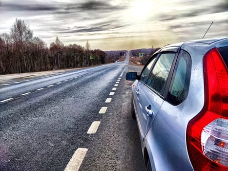 The car is on the side of the road. The concept of travel. A silver car stopped by the highway as daylight breaks